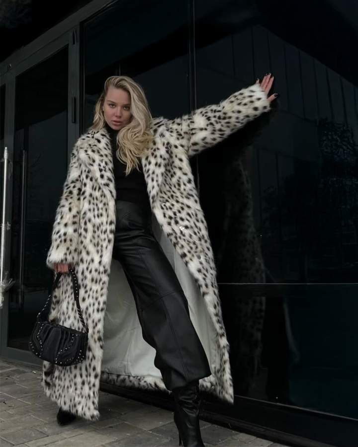 Person wearing a long leopard print coat in front of a dark building.
