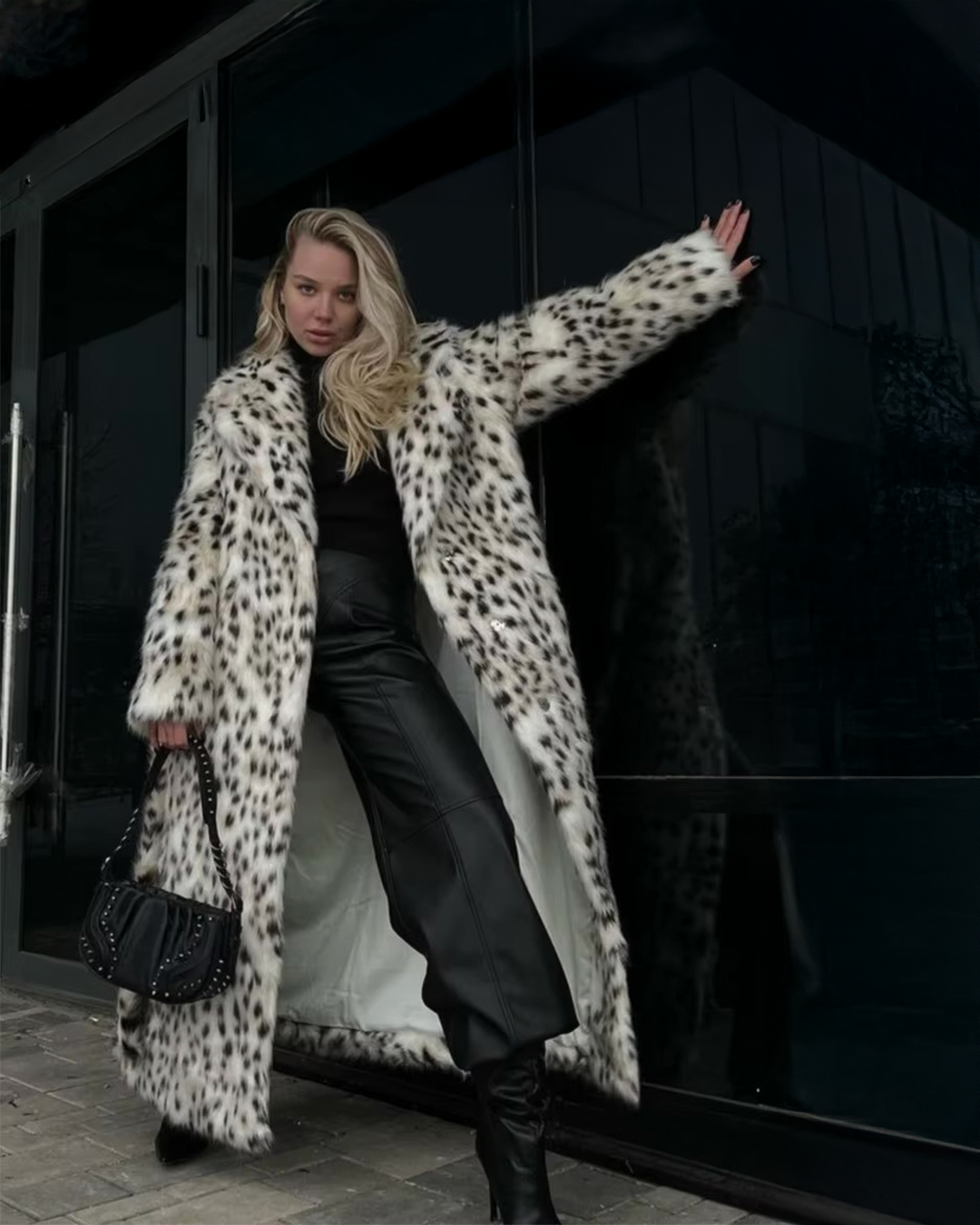 Person wearing a long leopard print coat in front of a dark building.