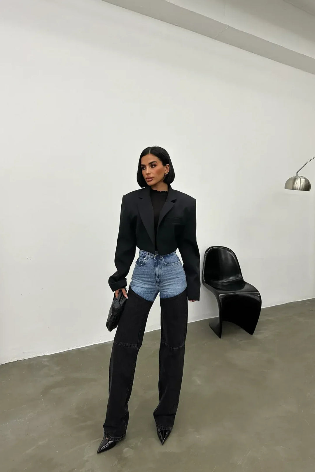 Woman wearing two-tone high-waist jeans, black blazer, pointed heels in minimalist room