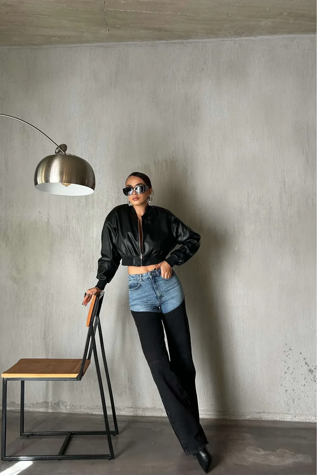 Woman in colorblock blue and black denim jeans, black cropped jacket, sunglasses, posing indoors