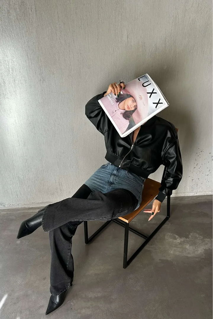 Woman in two-tone blue and black denim jeans, black faux leather jacket, pointed boots, sitting on chair