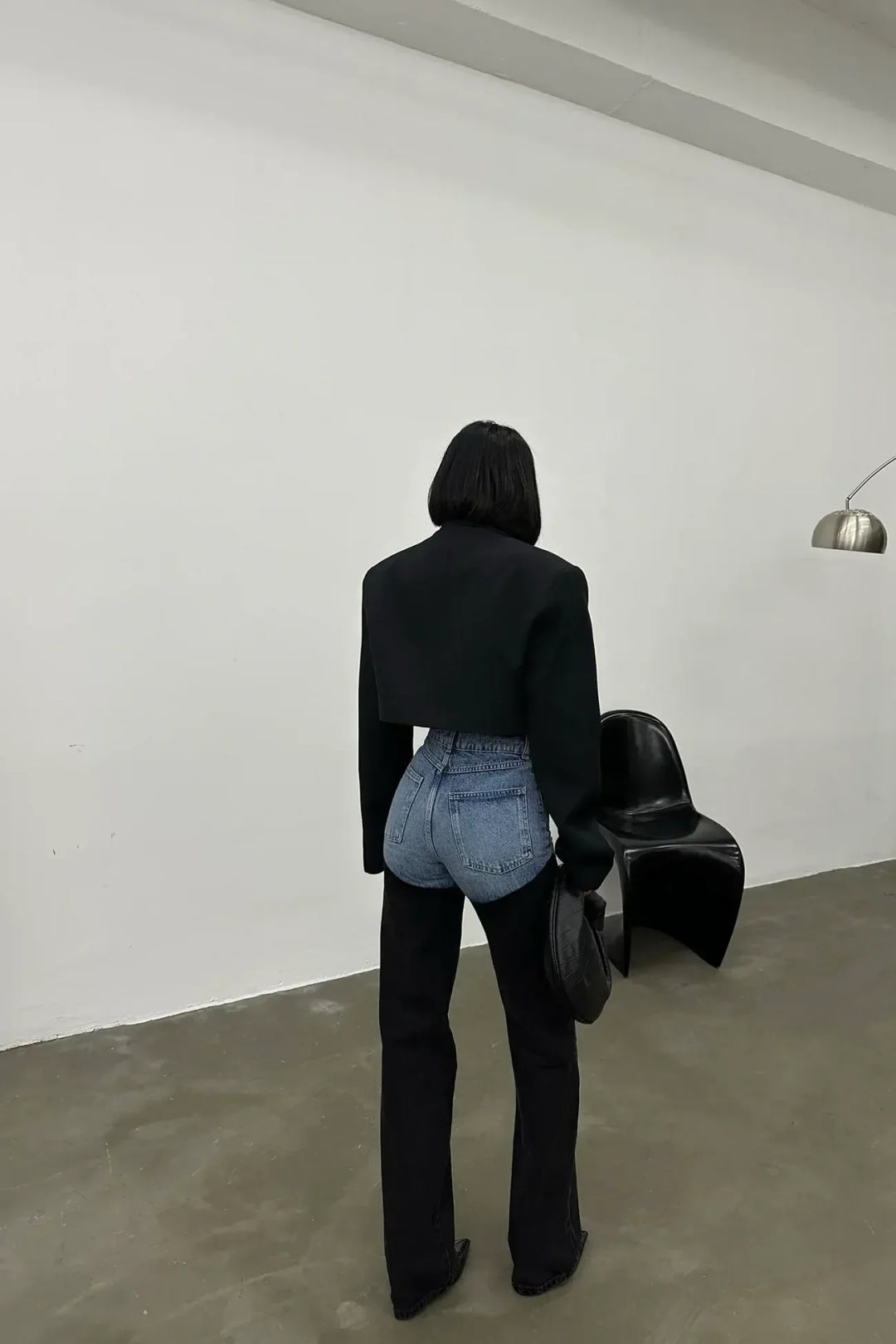 Woman in modern two-tone blue and black high-waisted jeans, cropped jacket, minimalist room