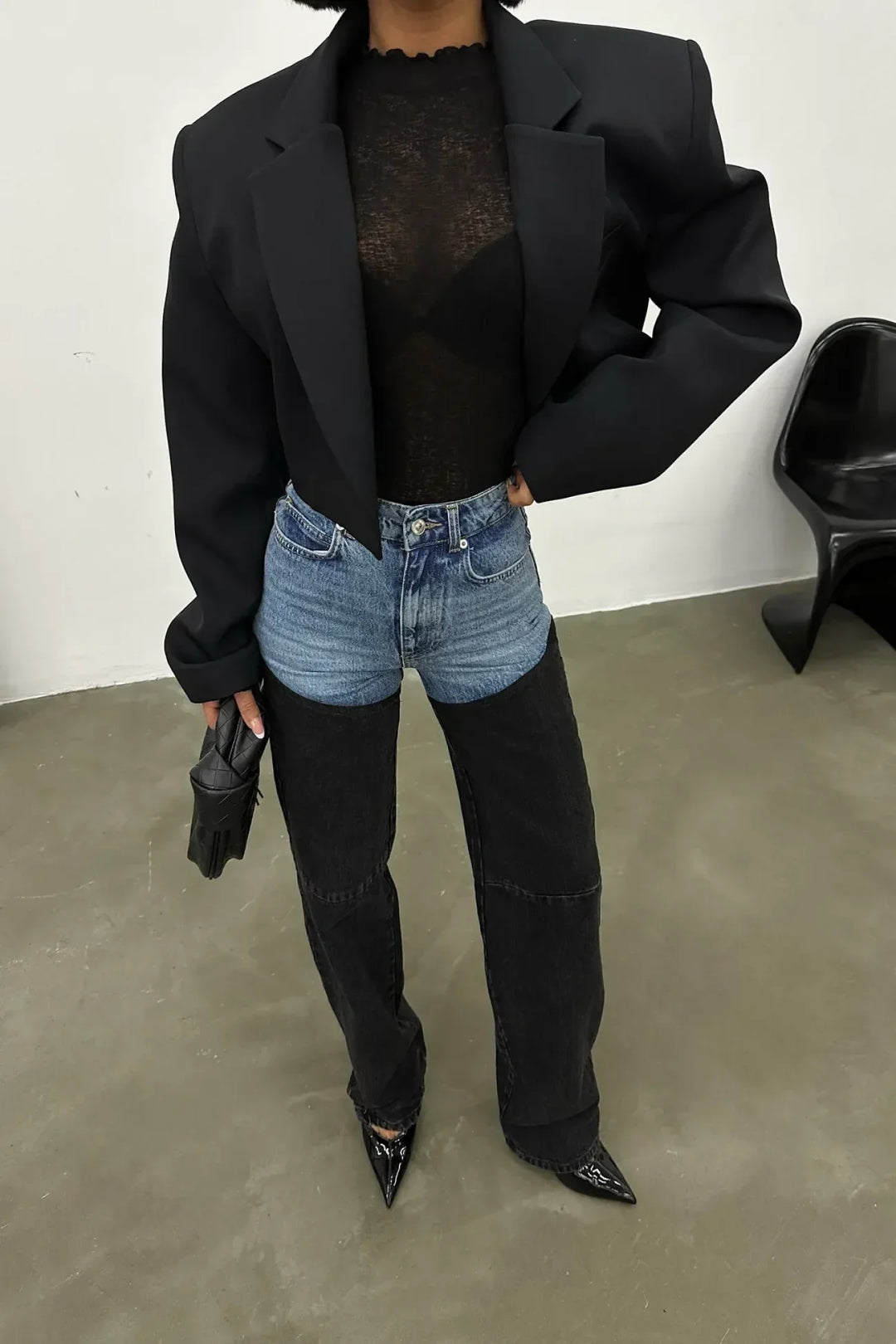 Woman wearing two-tone high-waisted denim jeans, black mesh top, cropped blazer, and pointed heels